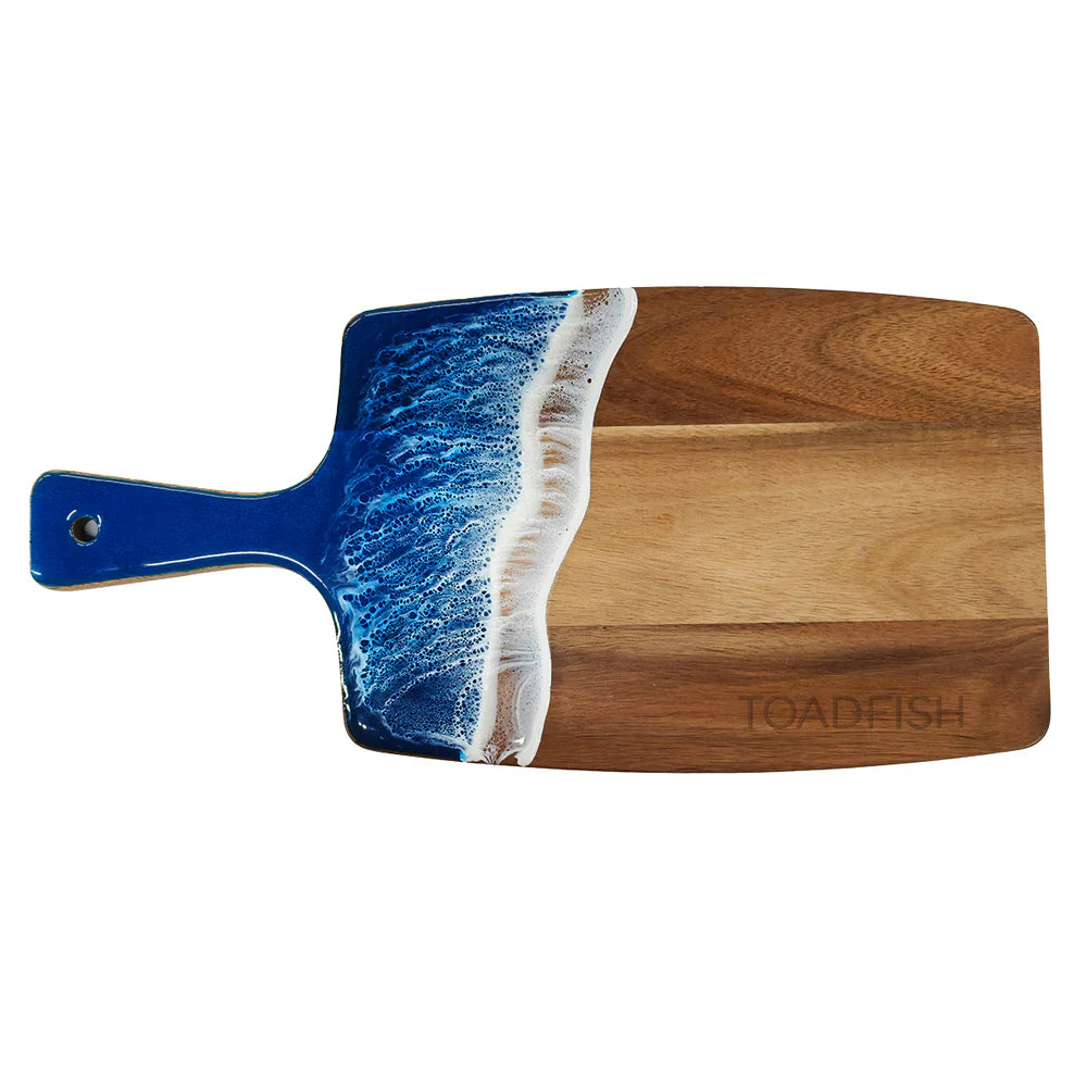 Wooden cutting board with blue resin ocean surf edge and 'Toadfish' branding on a white background.