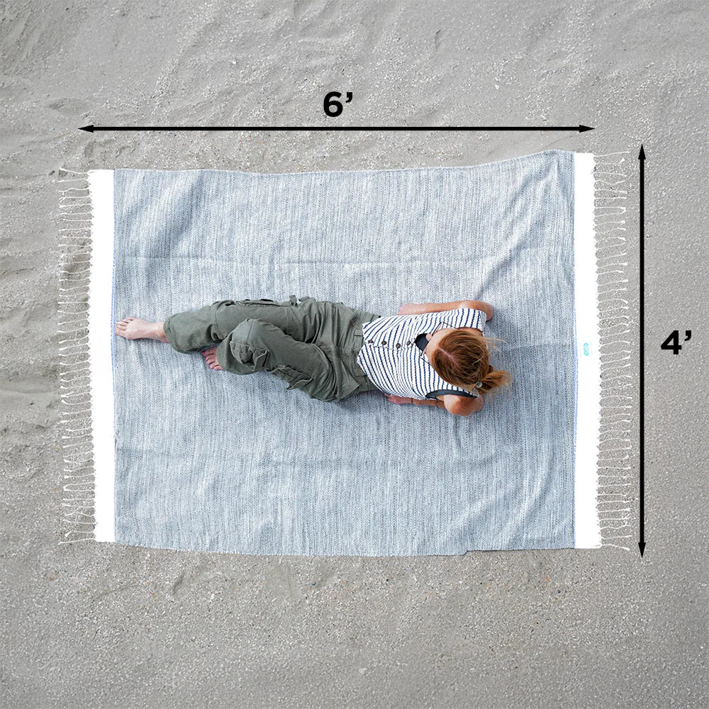 Person lying on a large blue and white striped towel with dimensions marked on a sandy surface.