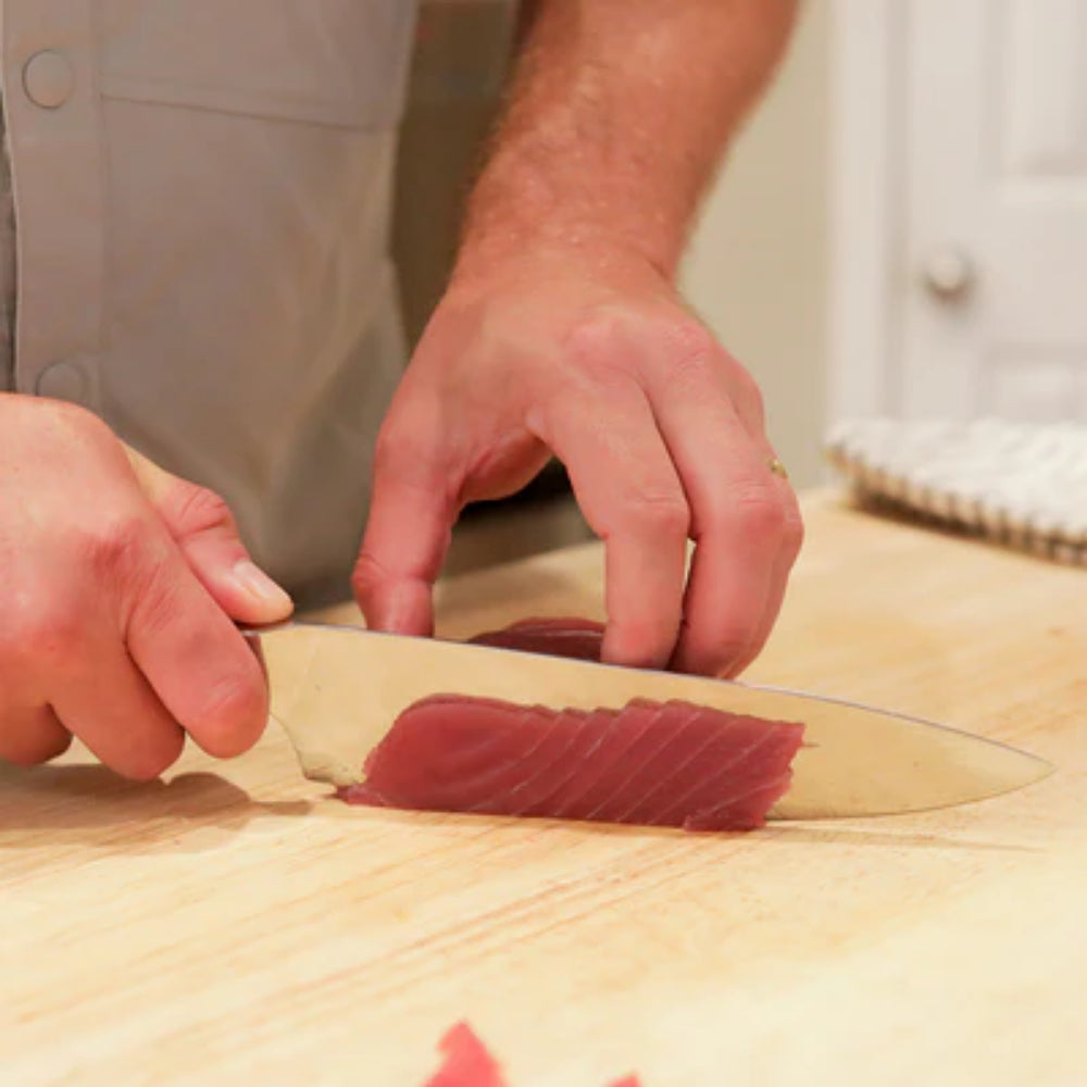 Person cutting raw fish on a wooden board with a knife.
