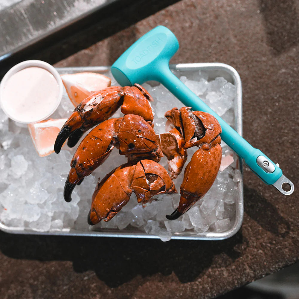 Crab claws on ice with a turquoise crab mallet in a metal tray.