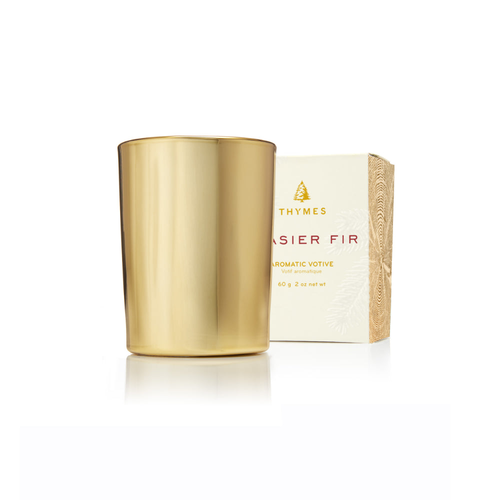 A gold metallic scented candle jar standing next to its cream-colored packaging box, which features the brand name 'Thymes' and the scent name 'Easier Fir'.