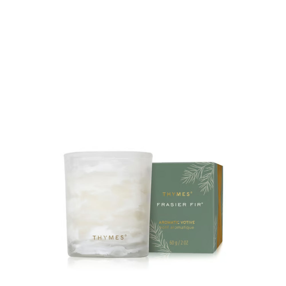 A frosted glass candle jar with a white wax surface next to its green and gold Thymes Frasier Fir packaging box, set against a plain white background.