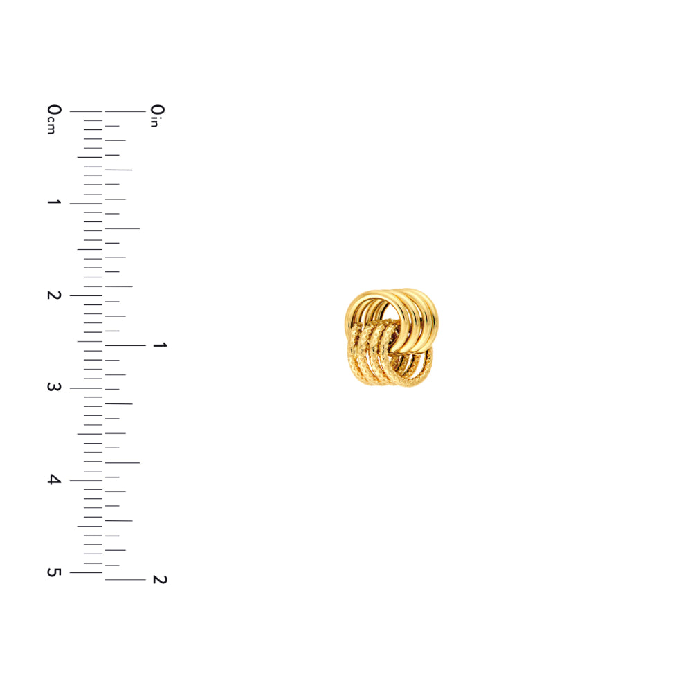 gold love knot stud earring on white background next to scale