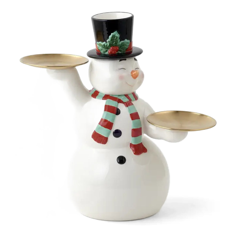 A white ceramic snowman figurine holding two gold-toned tray-like plates, wearing a black top hat with green holly and red berries, and a red and mint striped scarf.