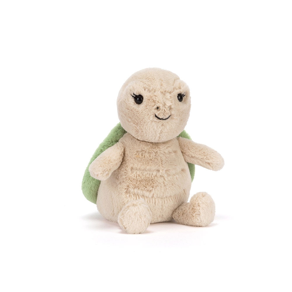 A photo of the side of a beige plush turtle toy with a smiling face and a green shell on a white background.