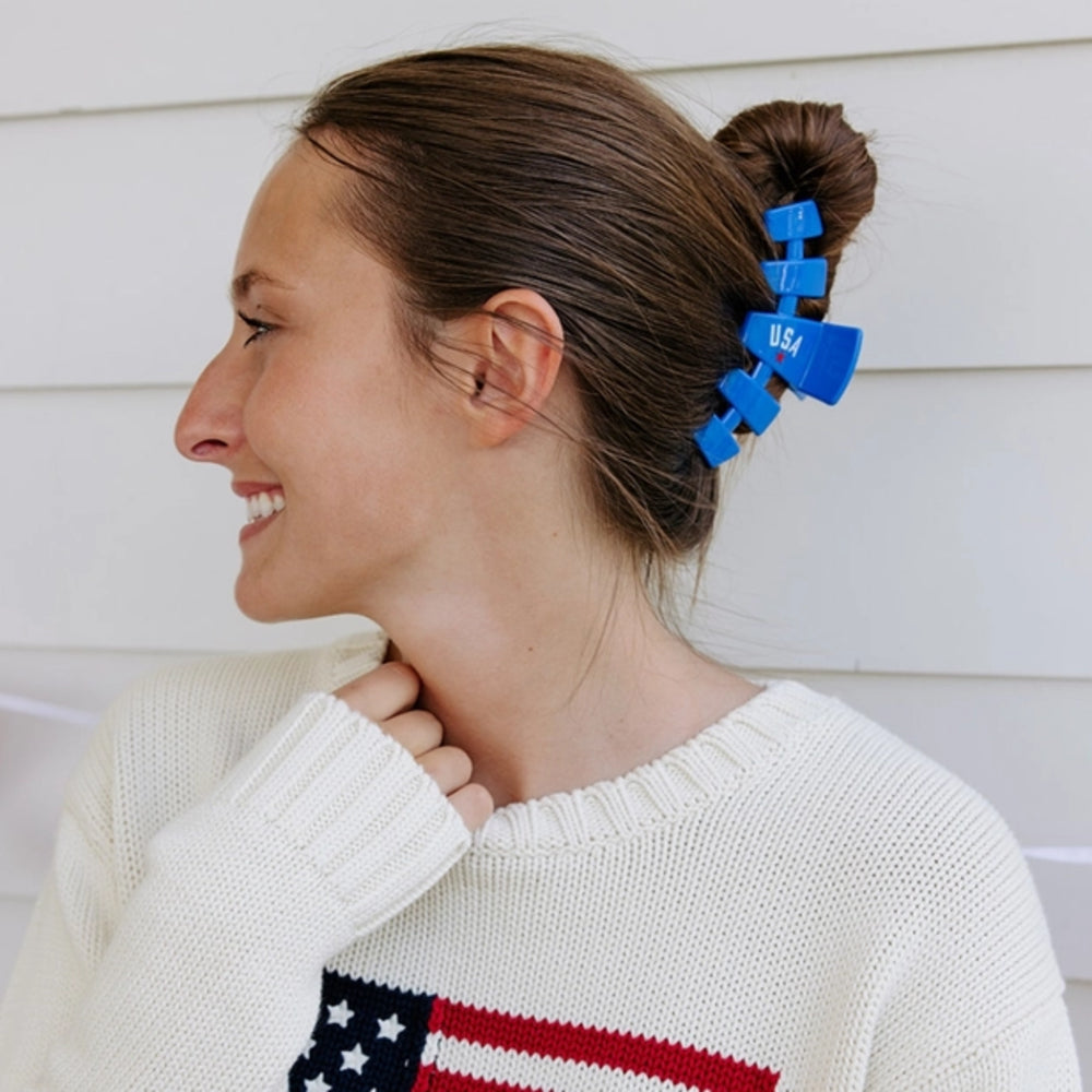 Woman with blue hair clips in her hair, wearing a white sweater with an American flag design.