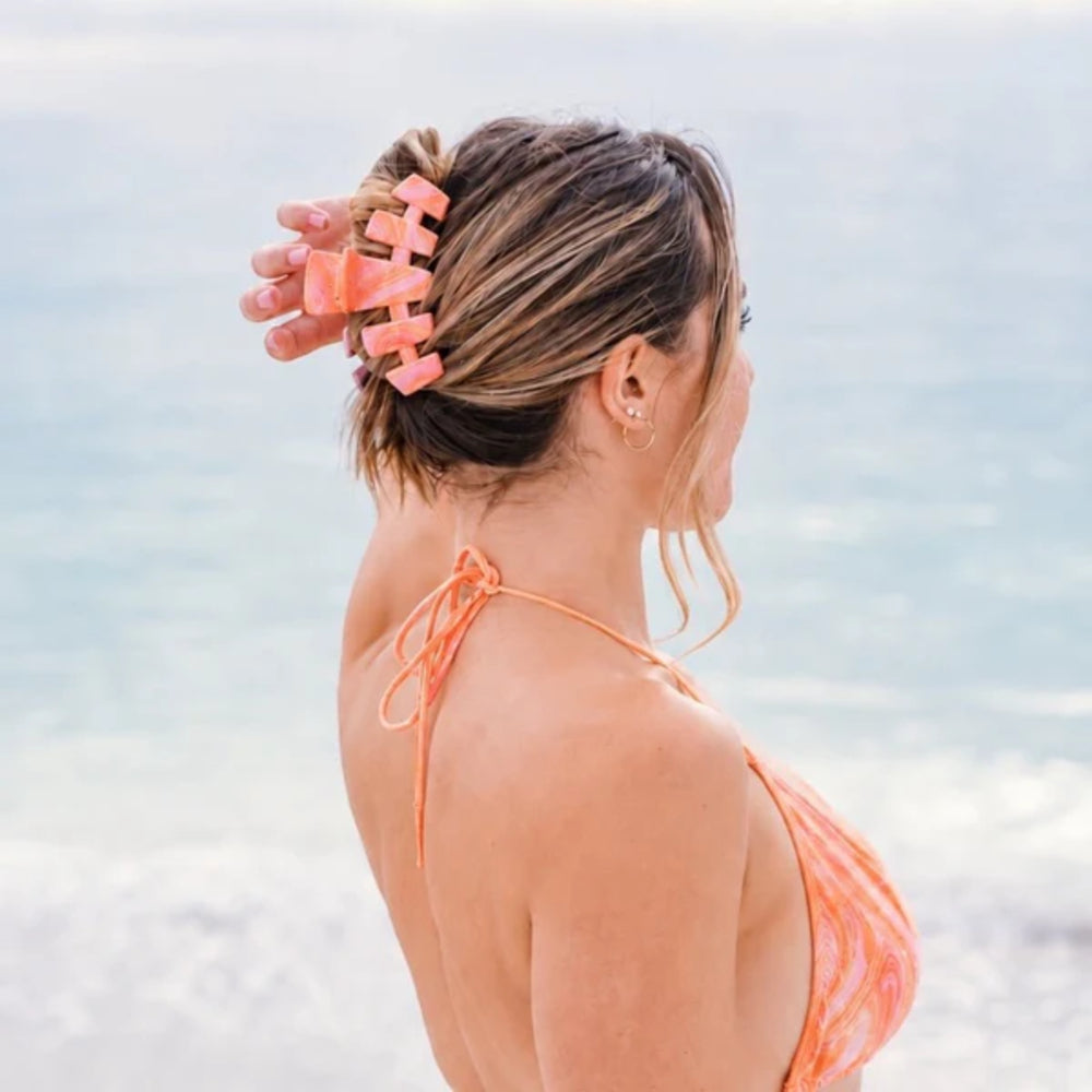 Woman wearing an orange bikini with a blurred beach background with pink marbled hair clip