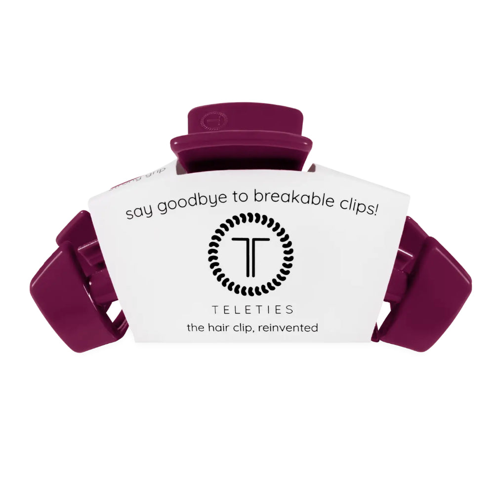 A purple hair clip with its white branded cardboard packaging insert, shown on a plain white background. The packaging features the brand name 'Teleties' and the slogan 'say goodbye to breakable clips!'.