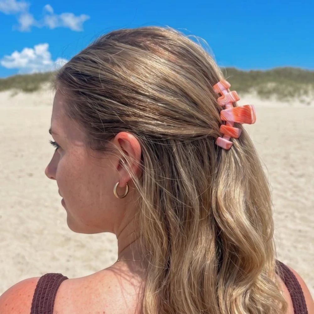 Woman with blonde hair tied back with a pink hair clip on a beach.