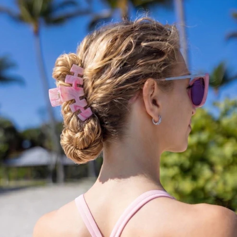 Woman with braided hair and pink sunglasses in a tropical setting