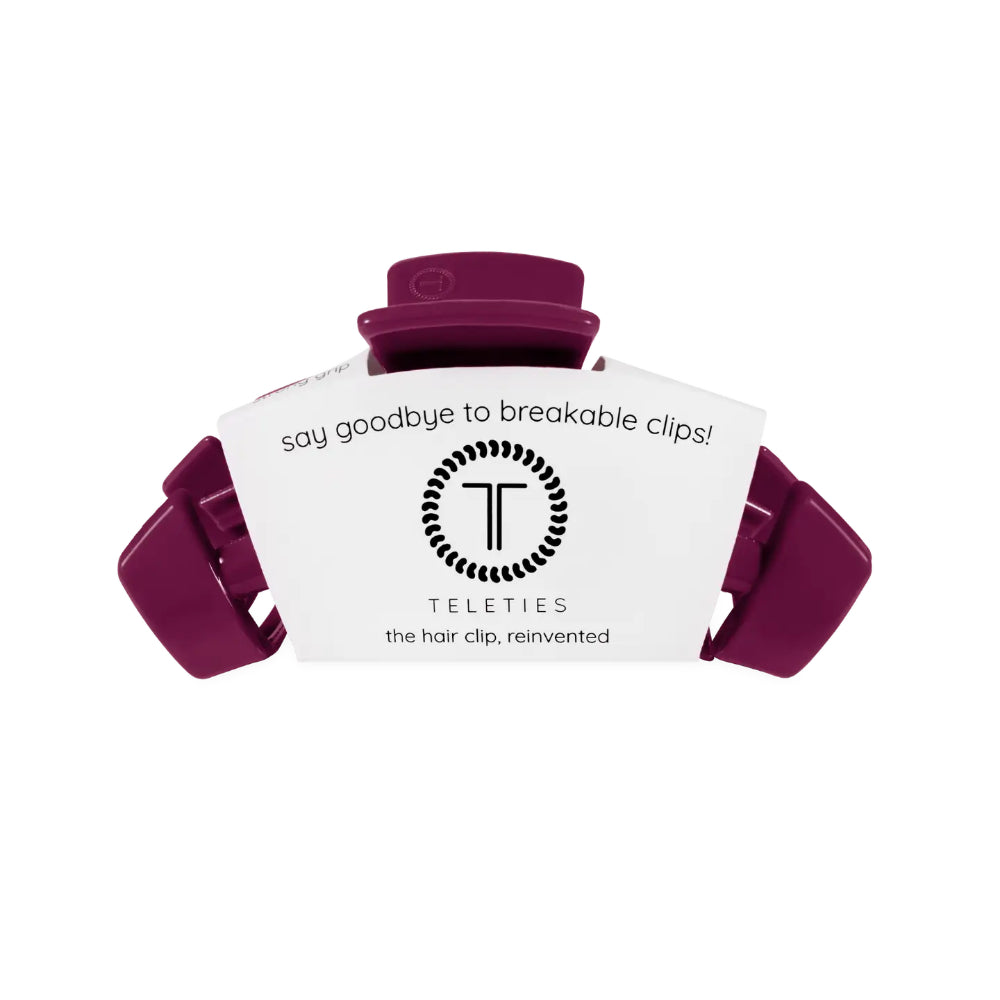 A purple hair clip with its white branded cardboard packaging insert, shown on a plain white background. The packaging features the brand name 'Teleties' and the slogan 'say goodbye to breakable clips!'.