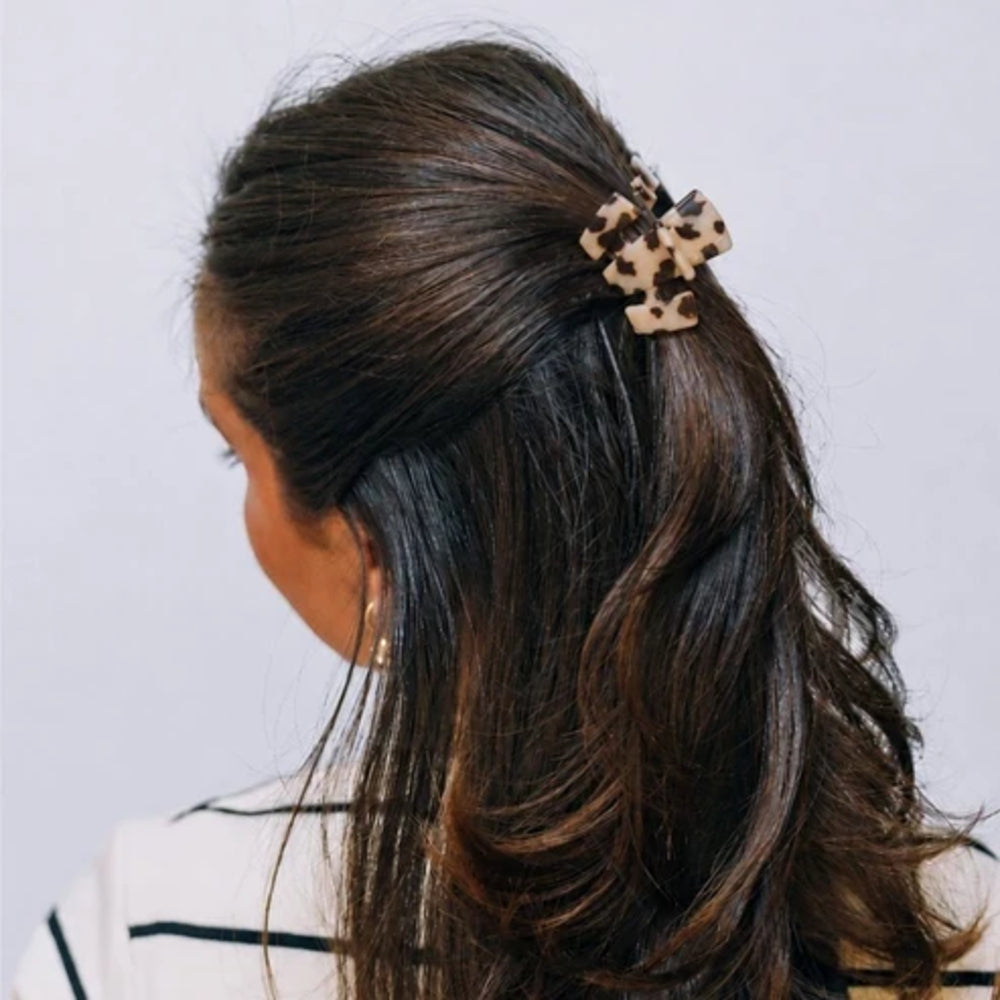 Person with long dark hair wearing a leopard print hair clip on a light gray background