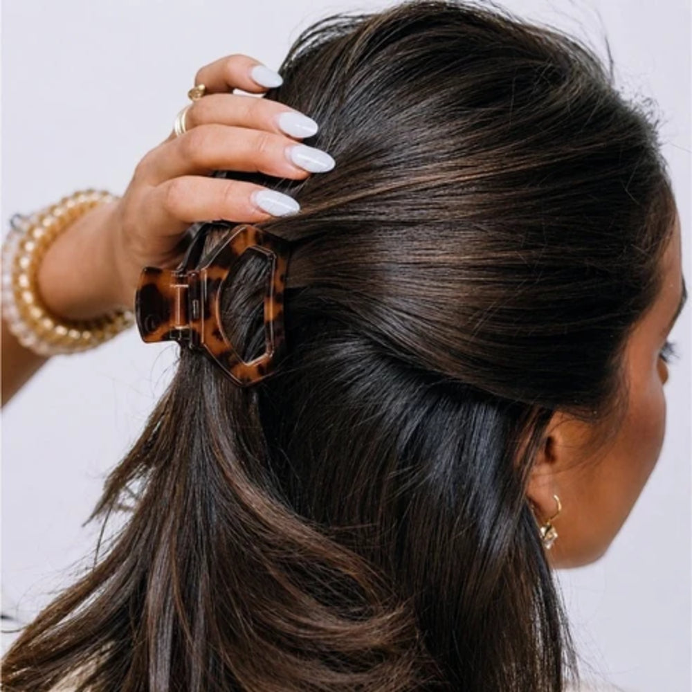Person styling hair with a tortoiseshell hair clip against a neutral background