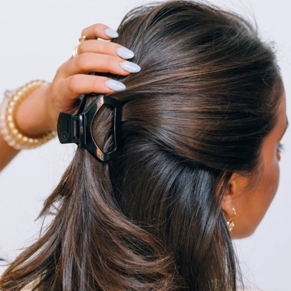 Person using a hair clip on their brown hair against a white background