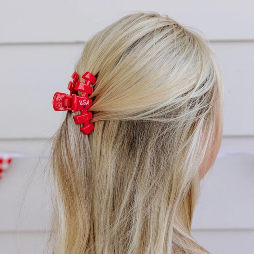 Red hair clip with 'USA' on a person's blonde hair against a neutral background