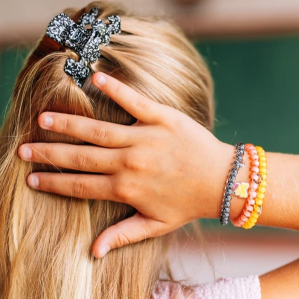 A close-up lifestyle shot of a person with long blonde hair wearing a black and white patterned hair claw clip and colorful beaded bracelets on their wrist.