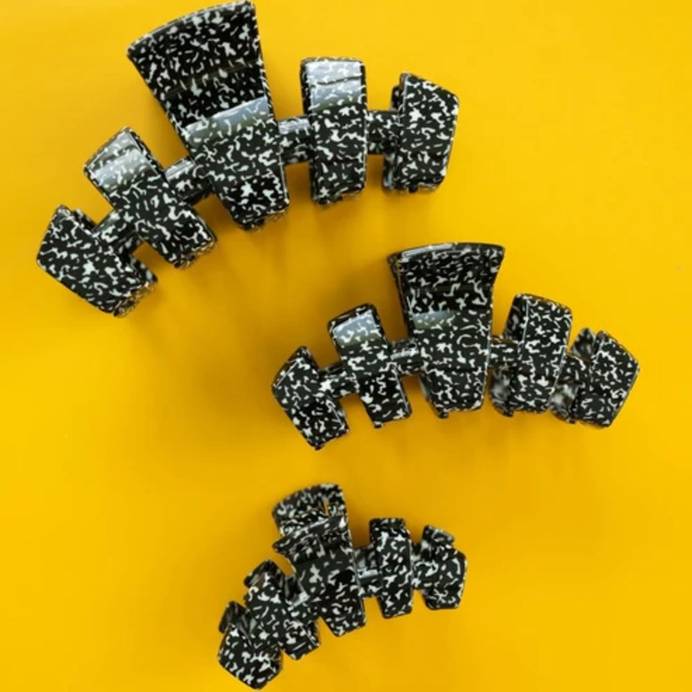 Three black and white speckled claw hair clips arranged on a bright yellow background.