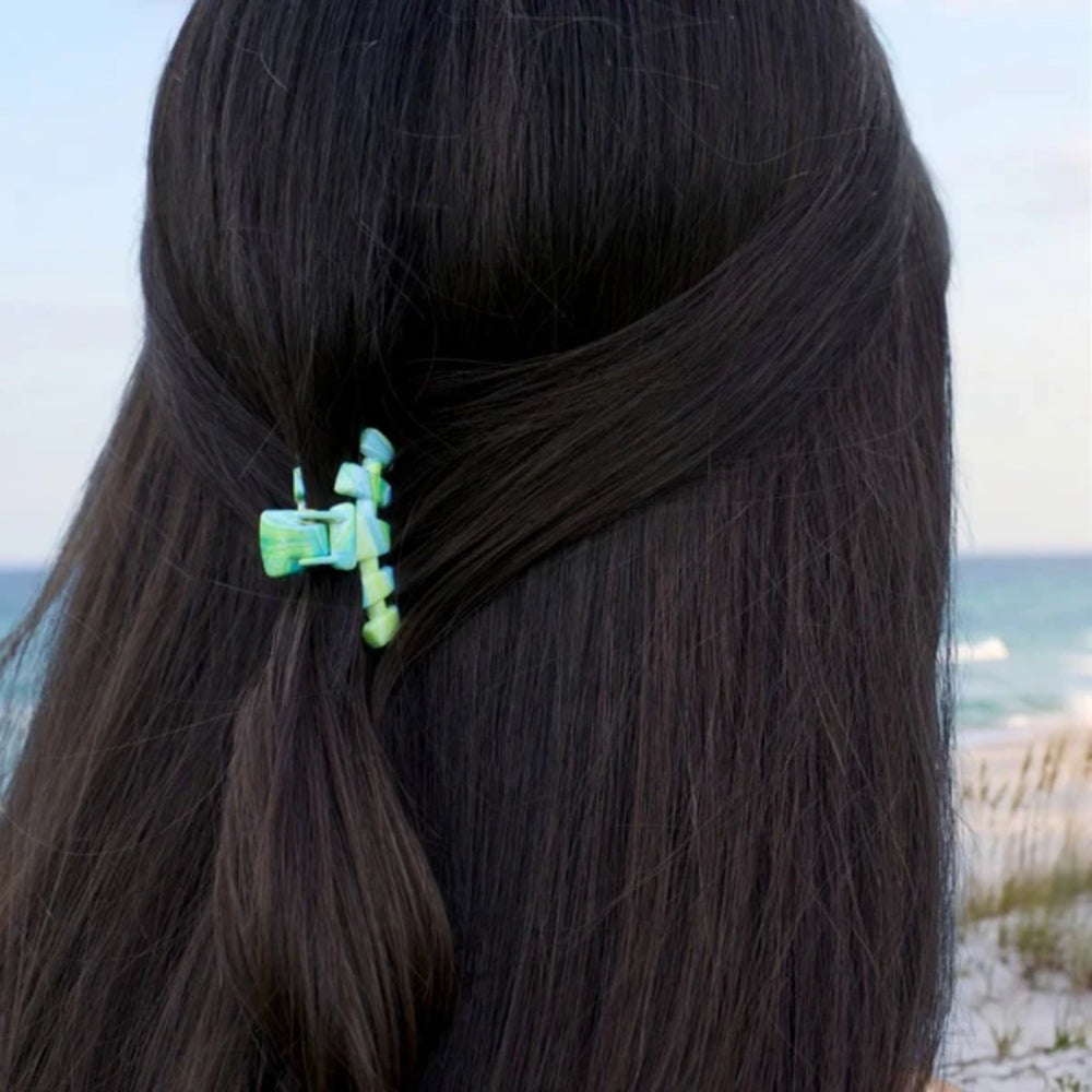 Close-up of a person with dark hair tied back with a green hair clip, beach in the background