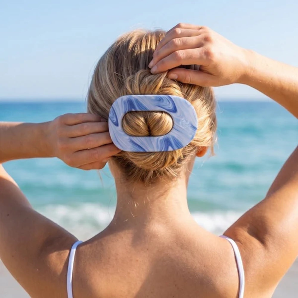 Person with a blue and white hair clip in their bun against a beach background