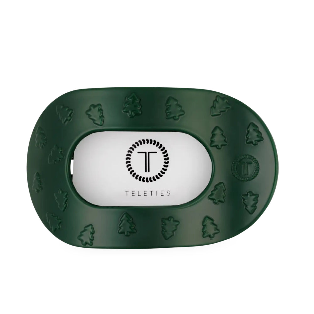A dark green hair clip with embossed tree and leaf patterns around the border and a white center insert featuring the Teleties logo.