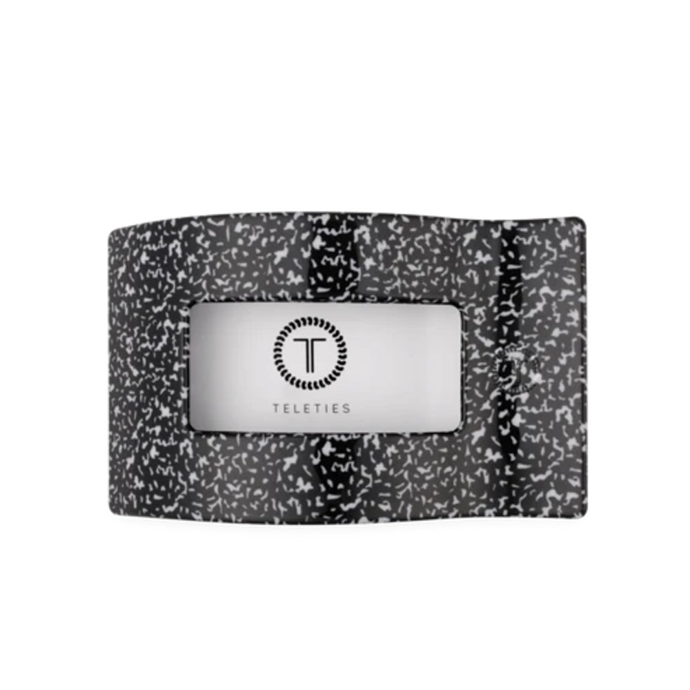 A black and white speckled silicone wristband with a central silver metallic badge featuring the Teleties logo and brand name.
