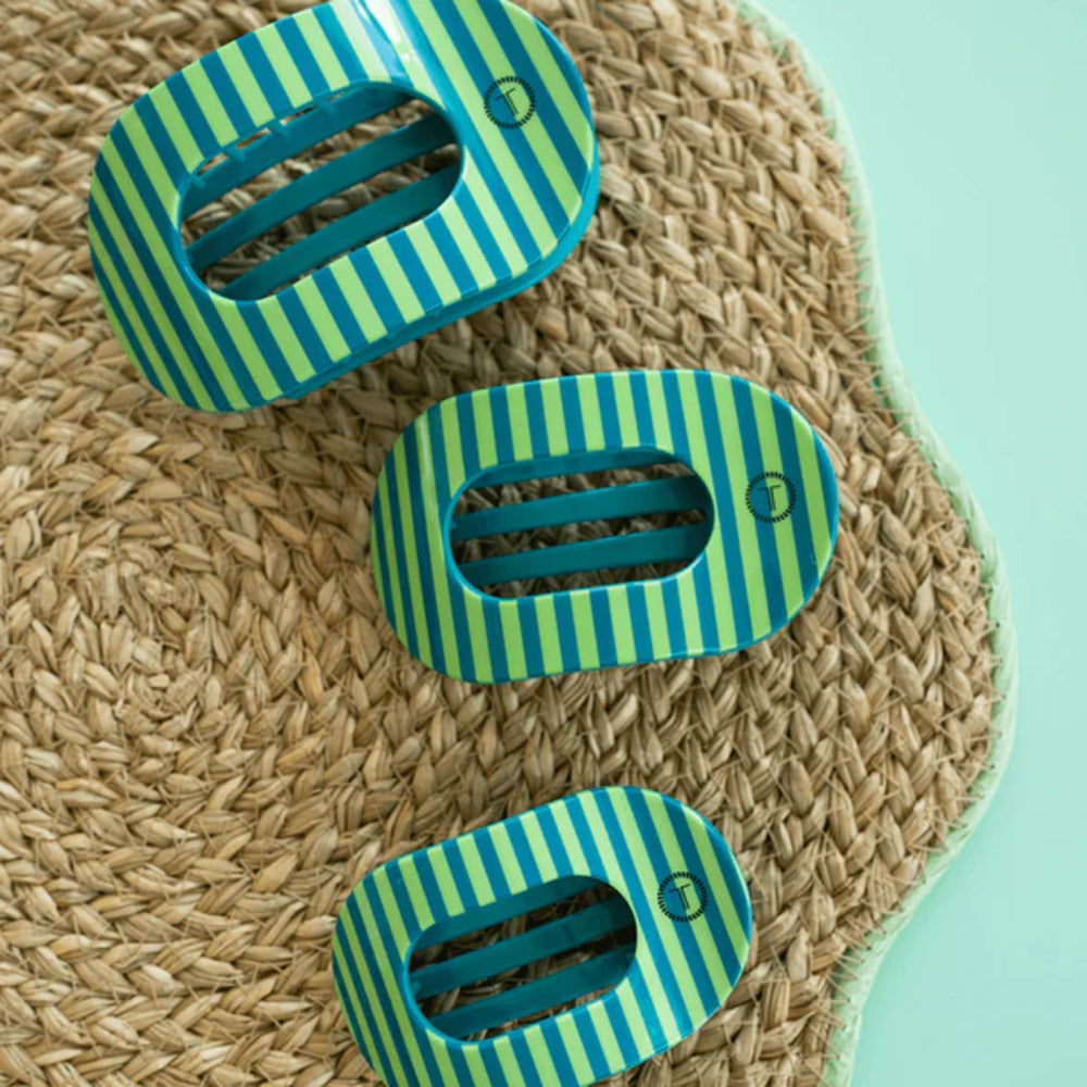Three green and blue striped clips on a woven mat with a light blue background