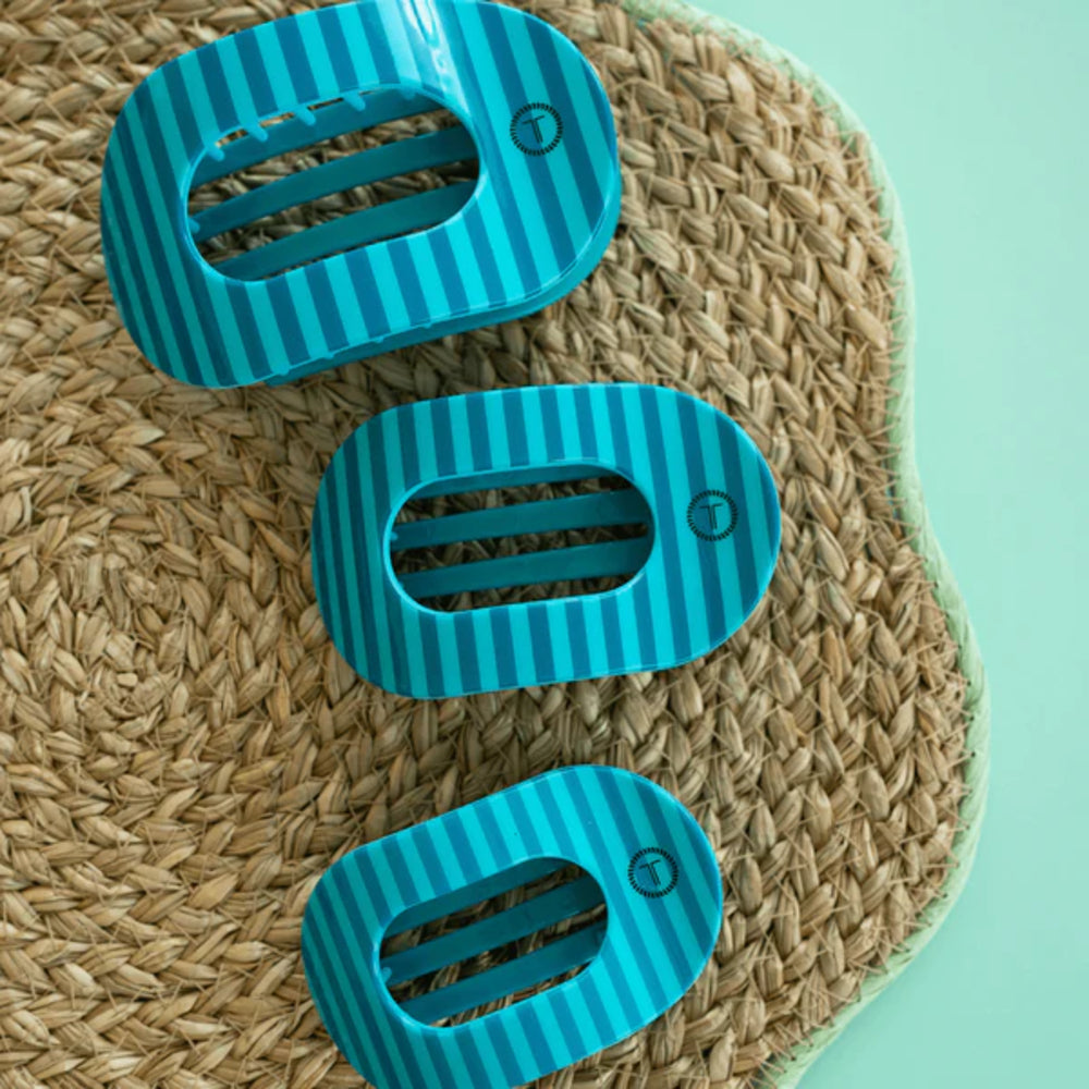 Three blue striped hair clips on a textured woven surface with a light green background