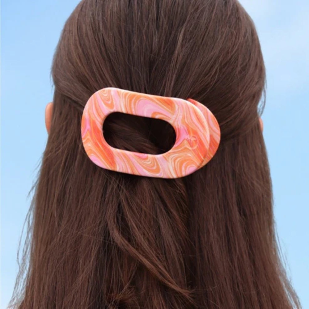 Marbled pink and orange hair clip on a person's head against a light blue background