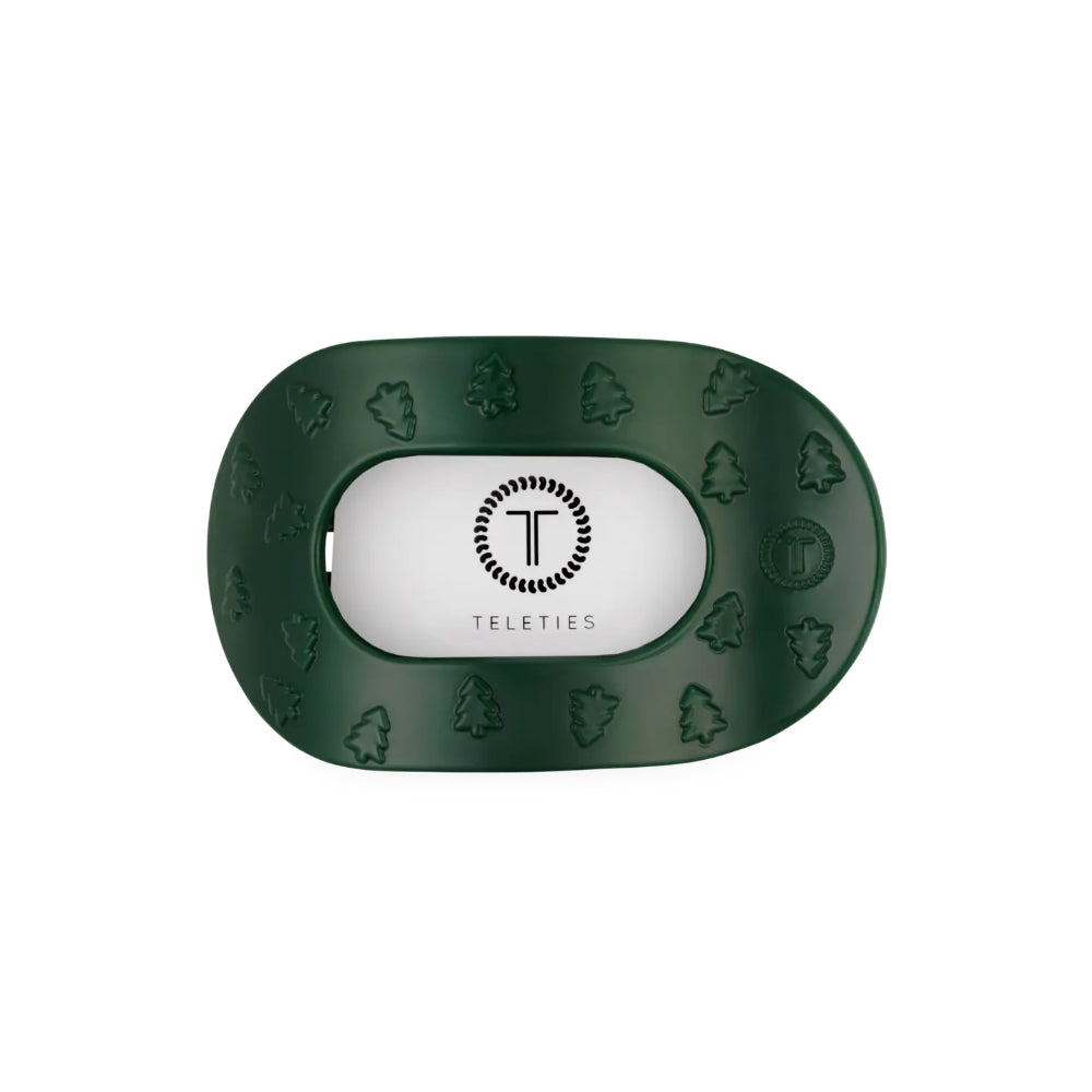 A dark green hair clip with embossed tree and leaf patterns around the border and a white center insert featuring the Teleties logo.
