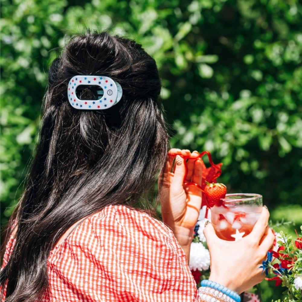 Person with a hair clip holding a drink outdoors