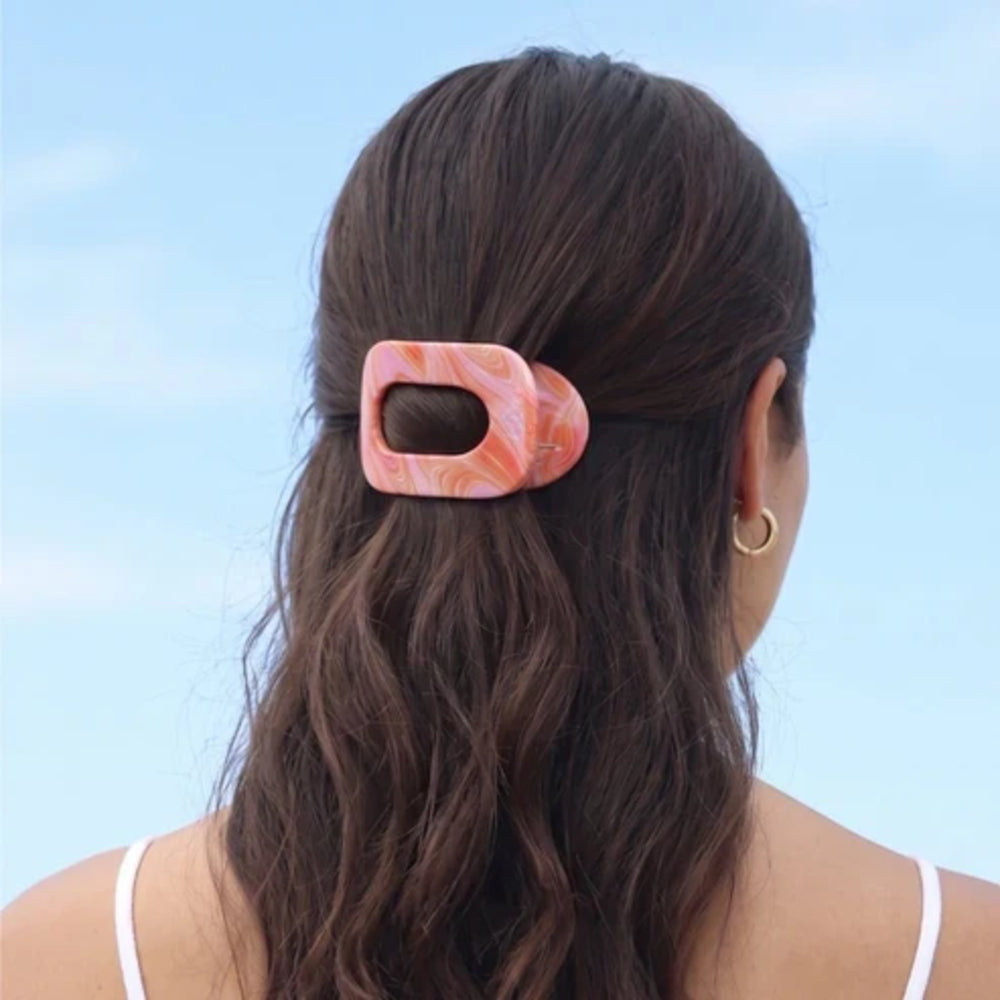 Person with a pink marble hair clip in their hair against a light blue background