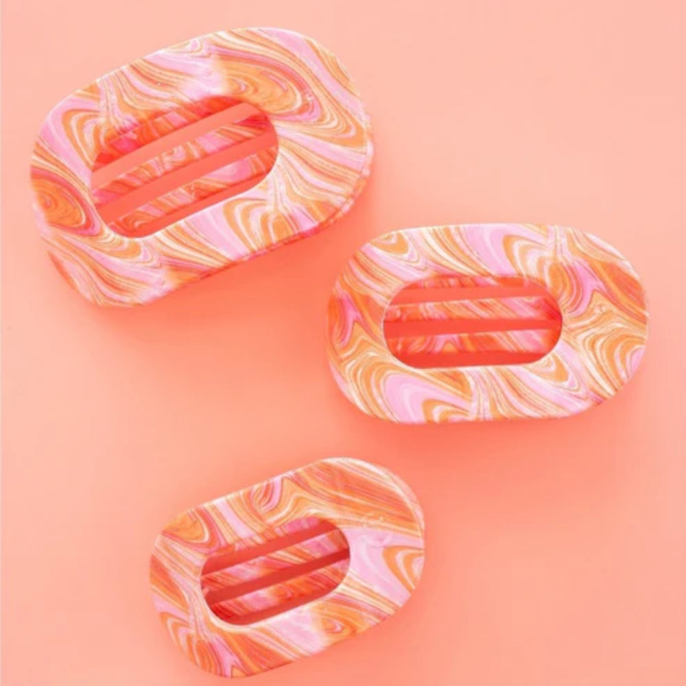 Three marbled pink and orange hair clips on a gradient pink background
