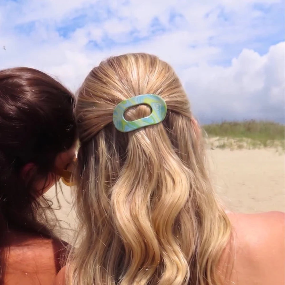 Two women on a beach with one wearing a hair clip.