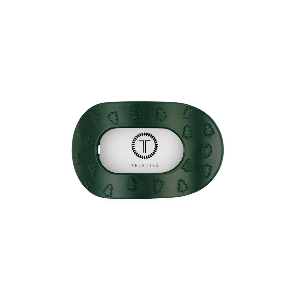 A dark green hair clip with embossed tree and leaf patterns around the border and a white center insert featuring the Teleties logo.