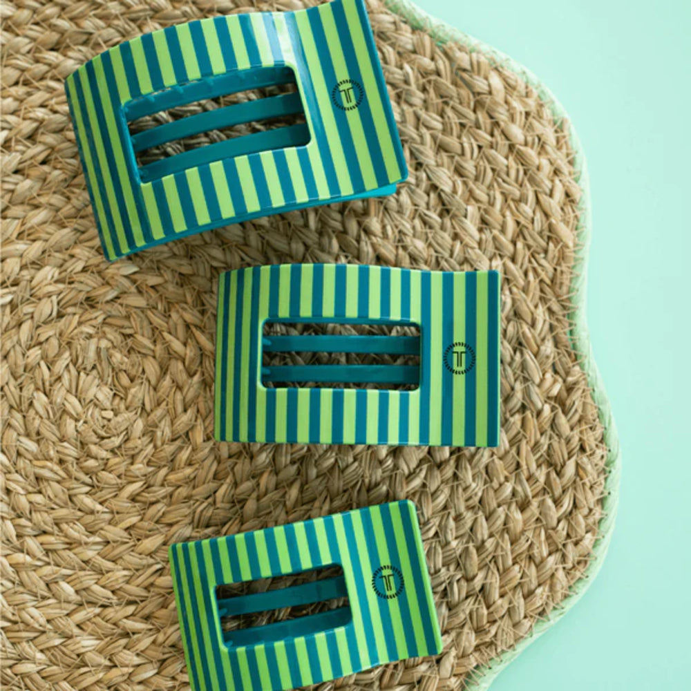 Three green and blue striped clips on a woven mat with a light blue background