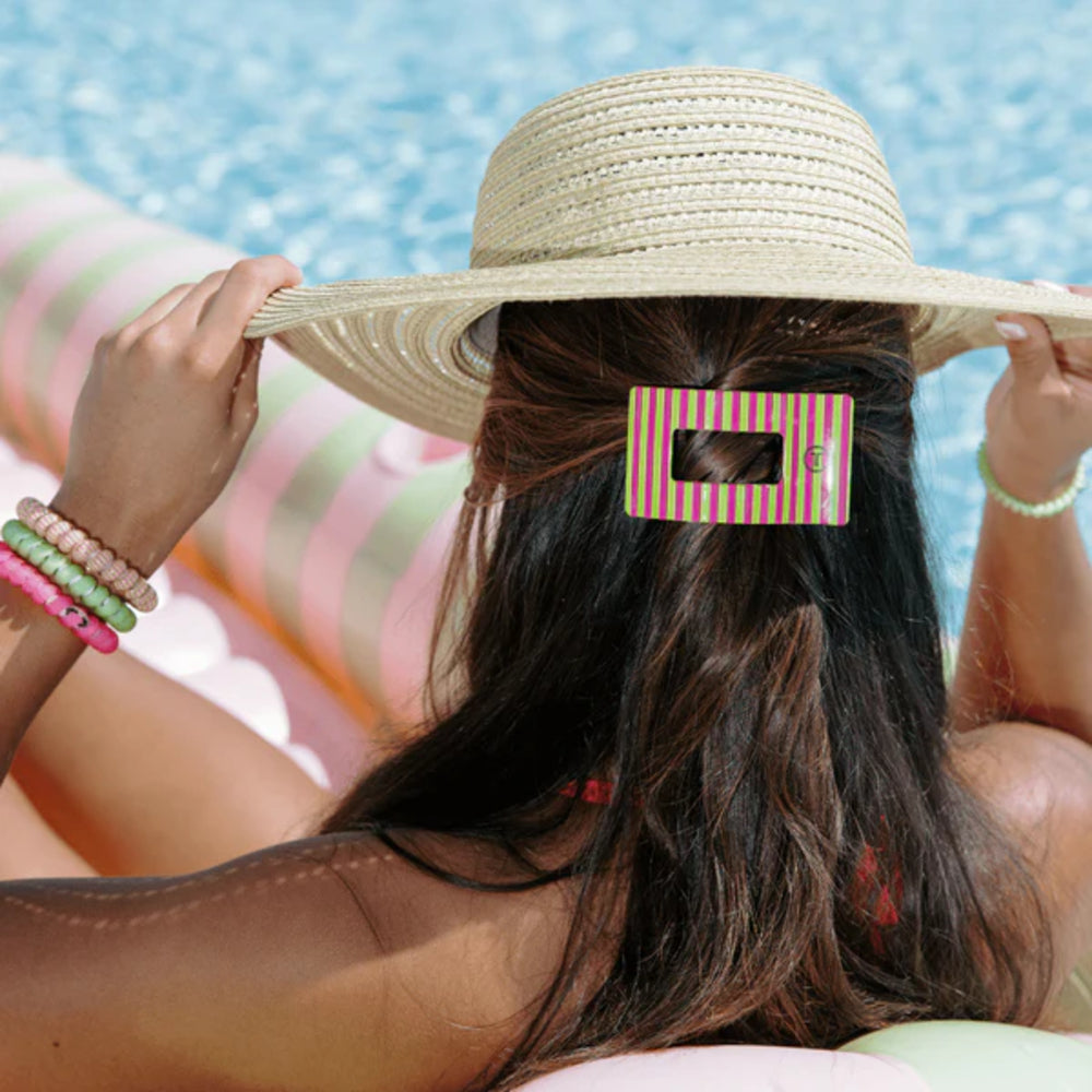 Person wearing a straw hat with a hair clip, sitting by a pool.