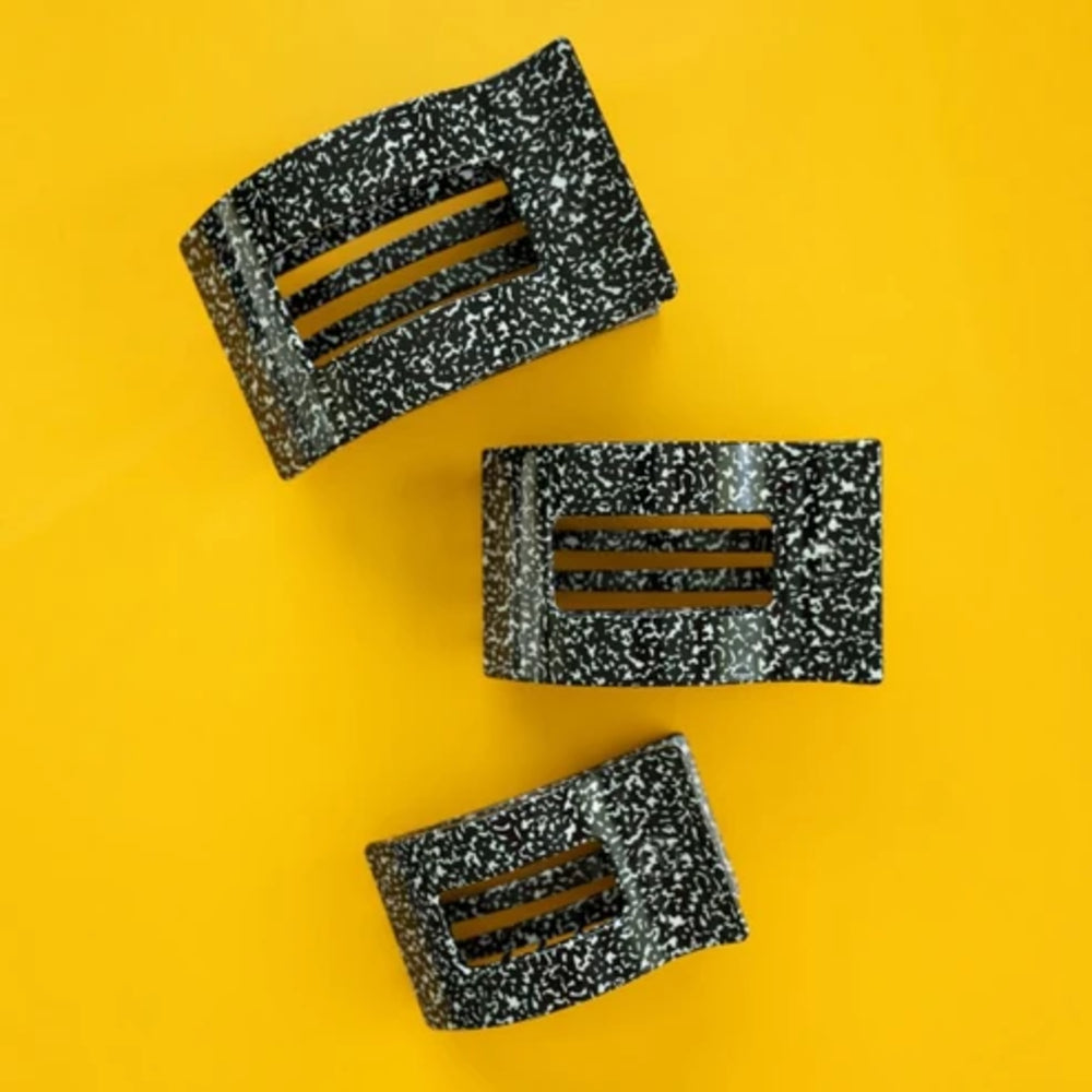 Three black and white speckled hair claw clips arranged diagonally on a solid yellow background.