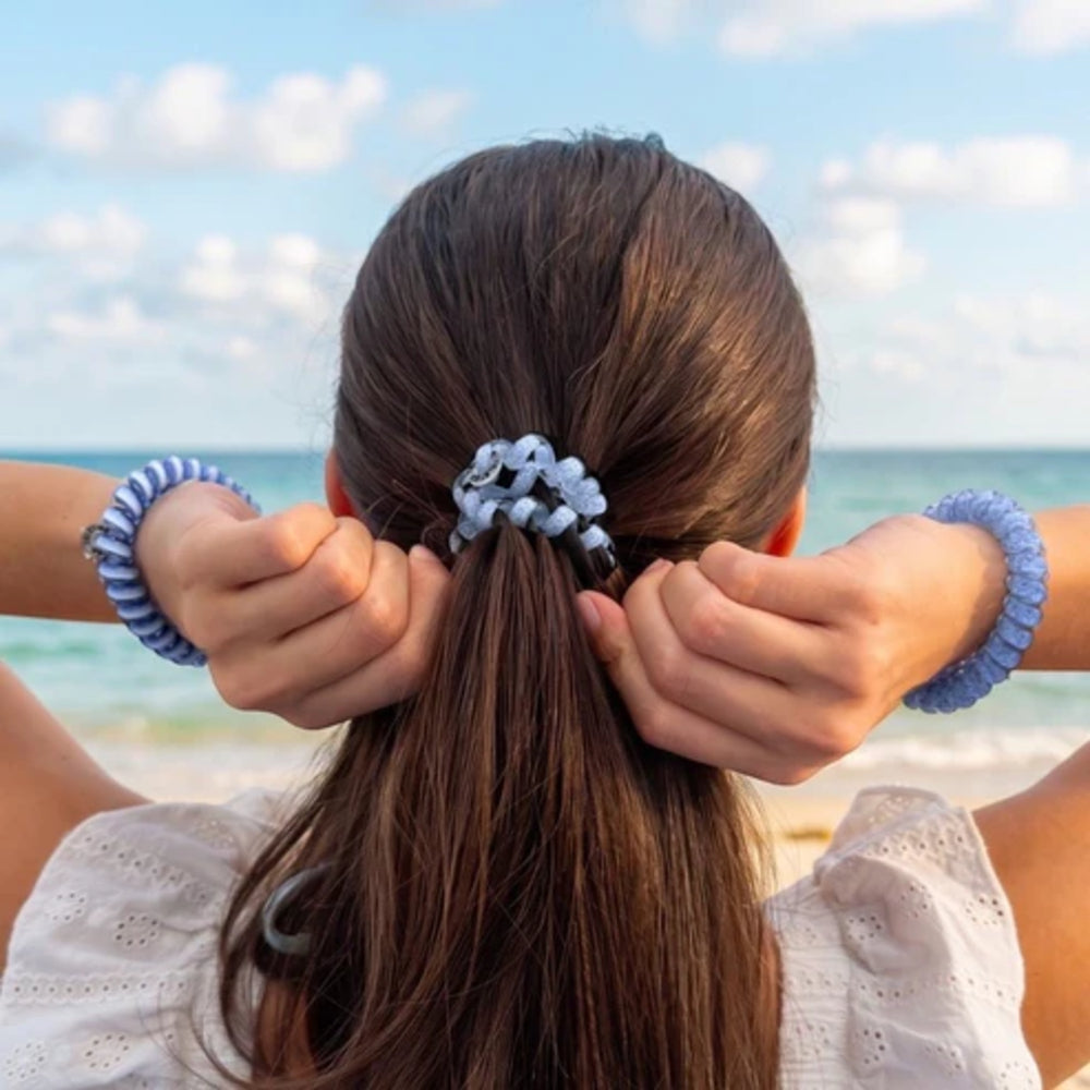 Person with hair tied back using blue hair ties by the ocean