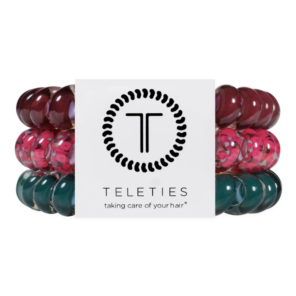 Three beaded hair extension bands in burgundy, pink, and teal, wrapped around a white Teleties brand card on a white background.