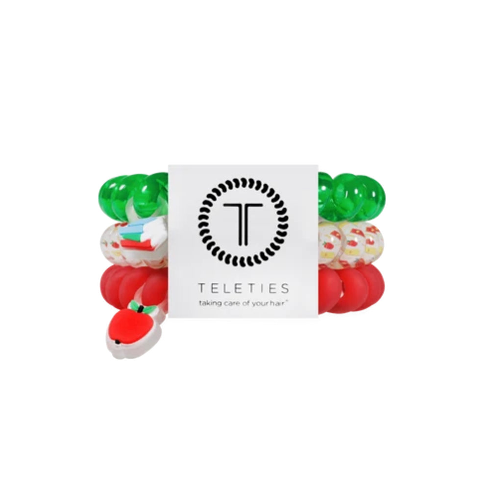 A set of Teleties baby hair stretch bands and a small apple-shaped teether, packaged with a white central card featuring the Teleties logo.