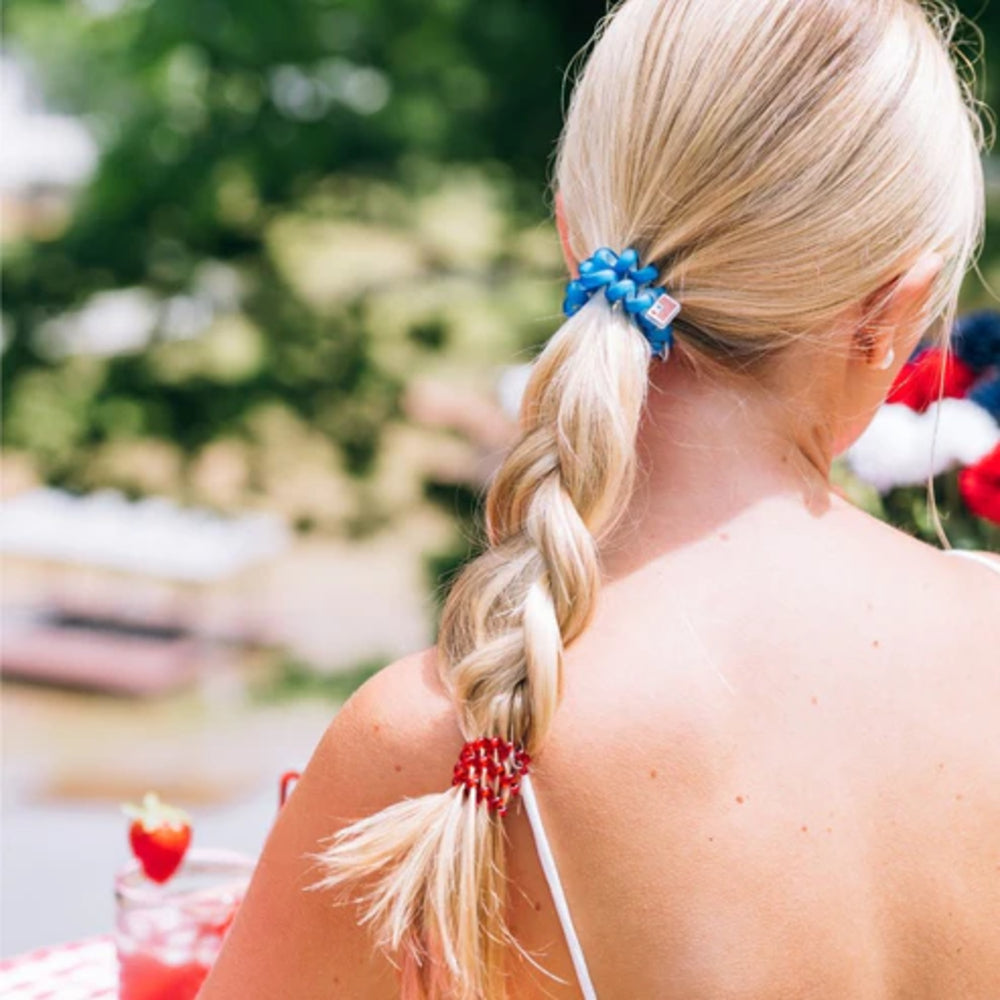Woman with braided hair wearing a blue hair tie with a red and white design, sitting outdoors.