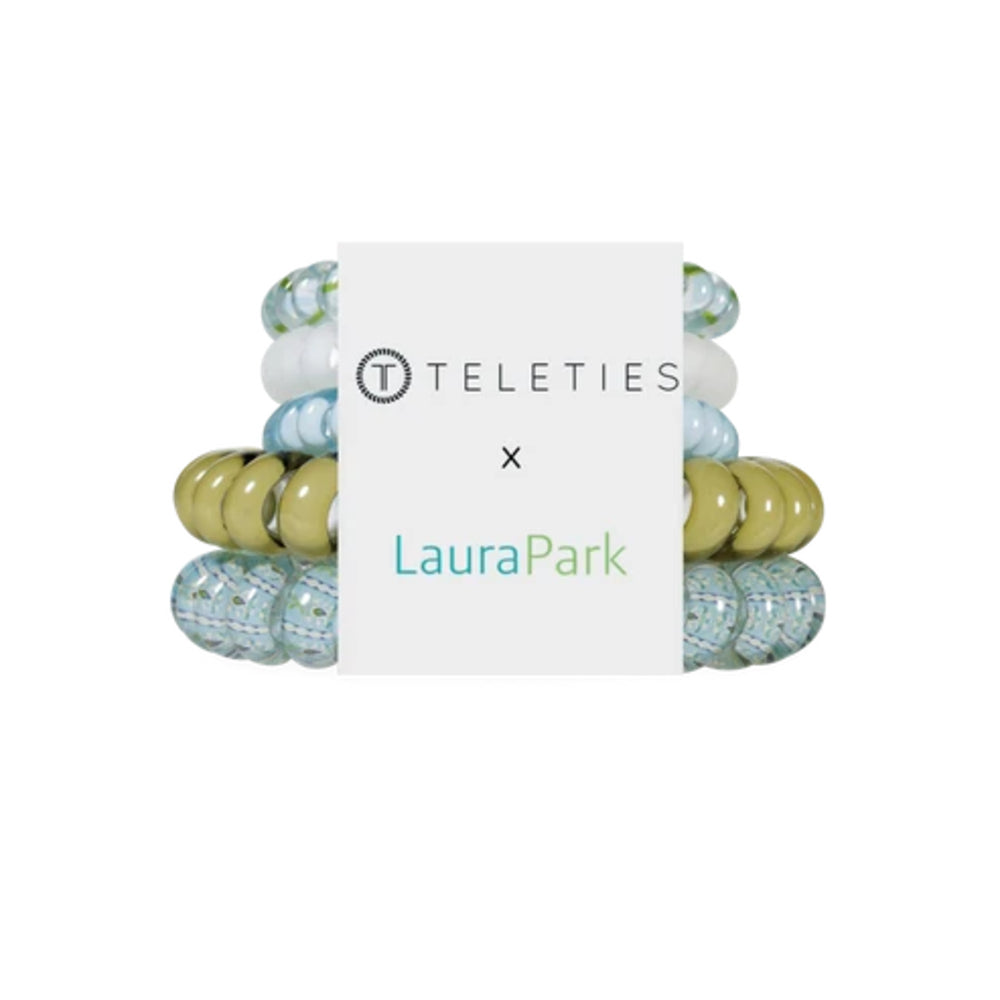 Four beaded stretch bracelets stacked behind a white paper band featuring the 'TELETIES x LauraPark' logo. The bracelets feature a mix of solid olive green, light blue and white marbled beads, and textured light blue beads.