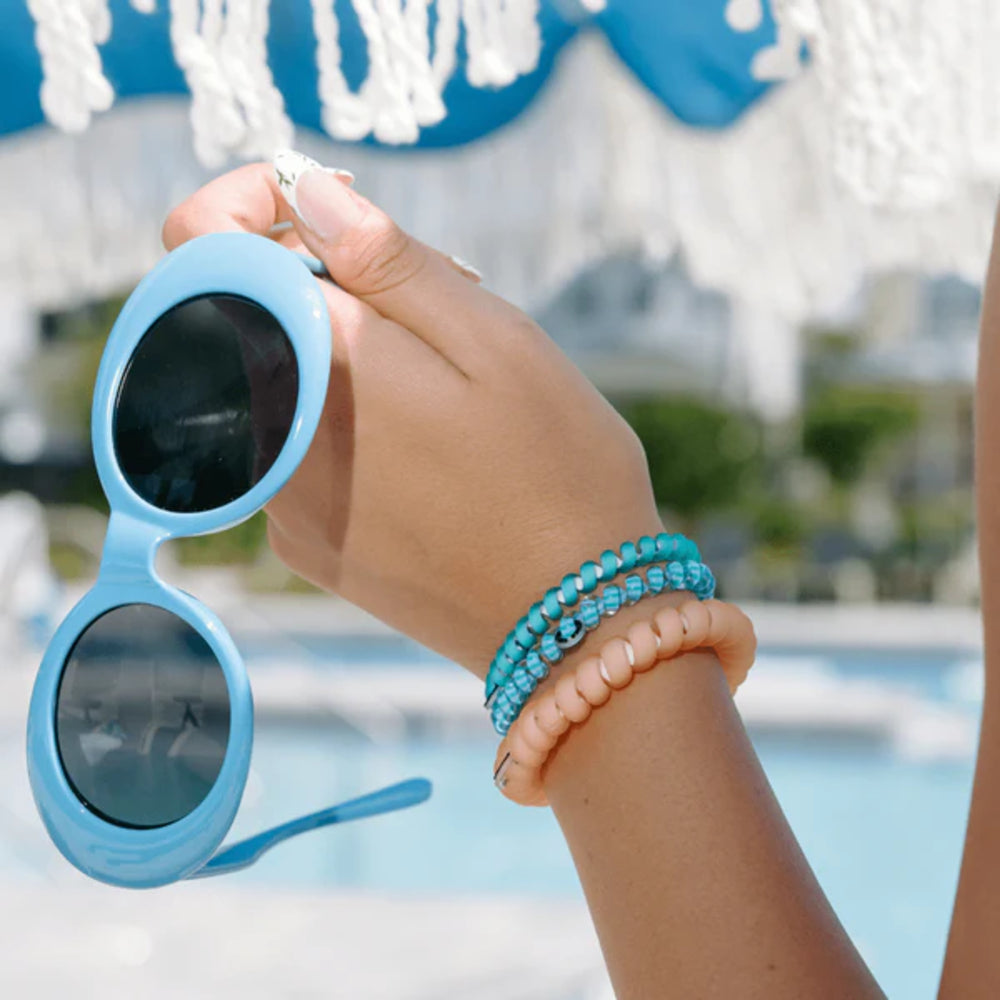Hand holding blue sunglasses with a pool and decorative elements in the background