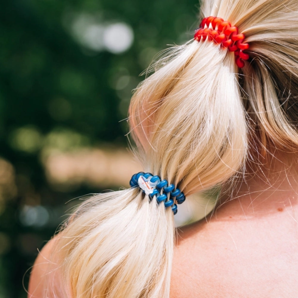 Close-up of a person's blonde hair tied with a red and blue hair tie against a blurred natural background.