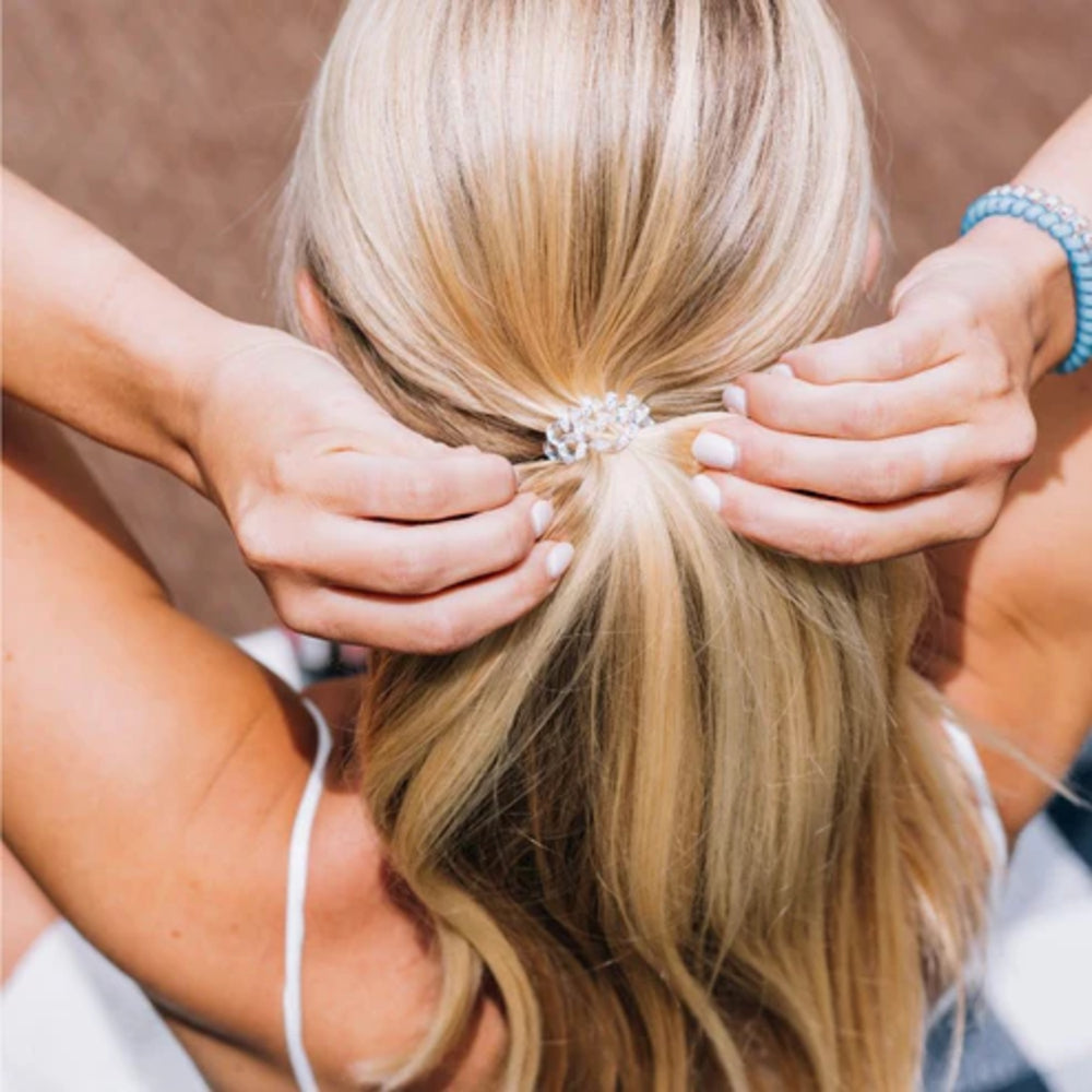 Person adjusting a hair bun with a decorative hair accessory.