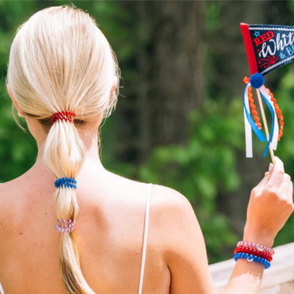 Person with blonde hair in a ponytail holding a festive flag with red, white, and blue colors.