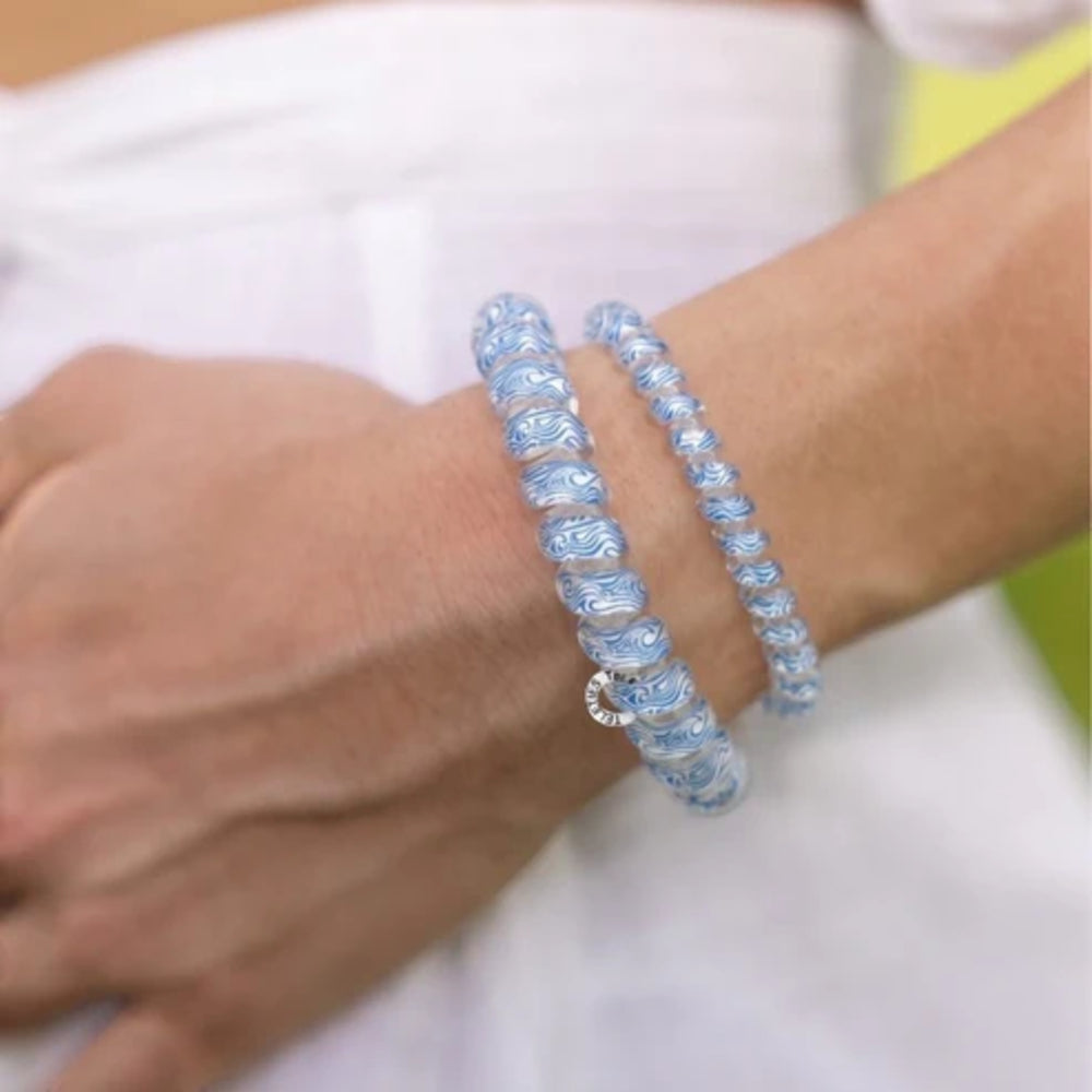 Close-up of a wrist wearing two blue beaded hair ties on a blurred background