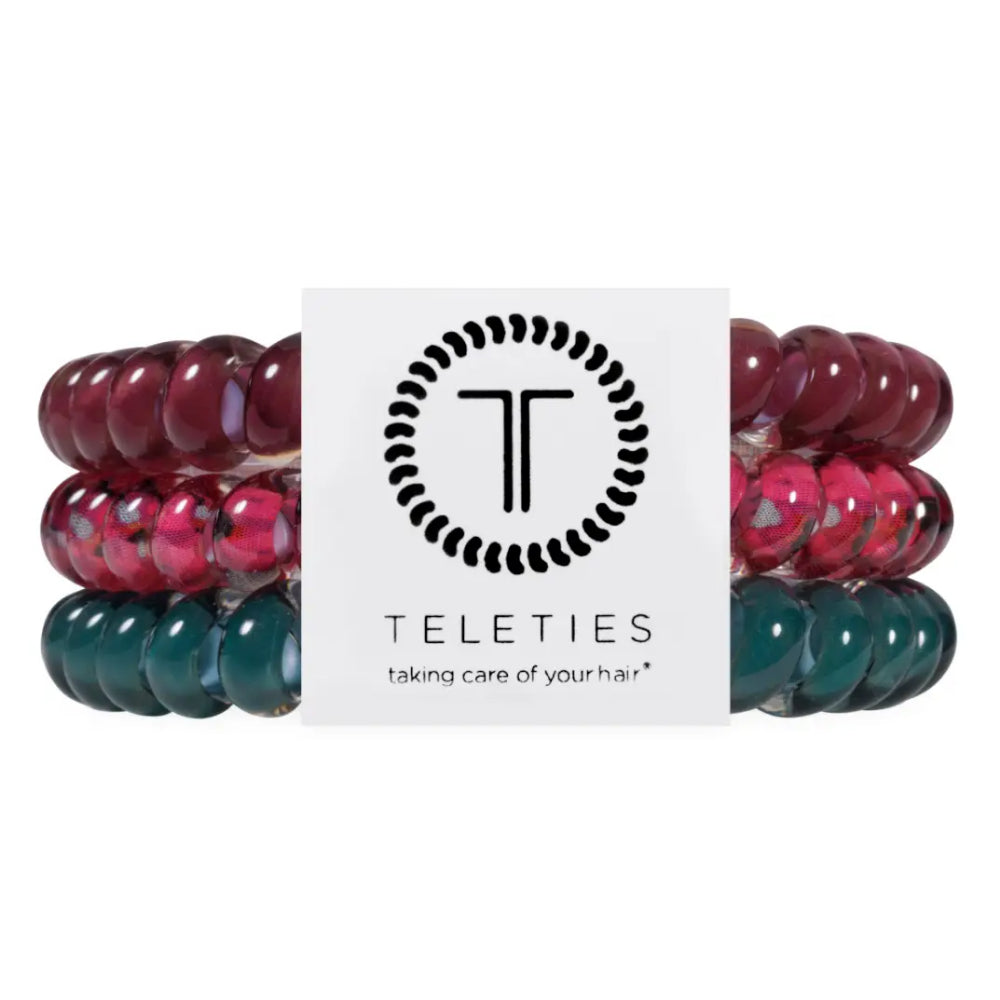 Three beaded stretch bracelets by Teleties, stacked behind a white brand card. The bracelets feature glossy dark red, translucent pink-and-red marbled beads, and deep teal-green marbled beads.
