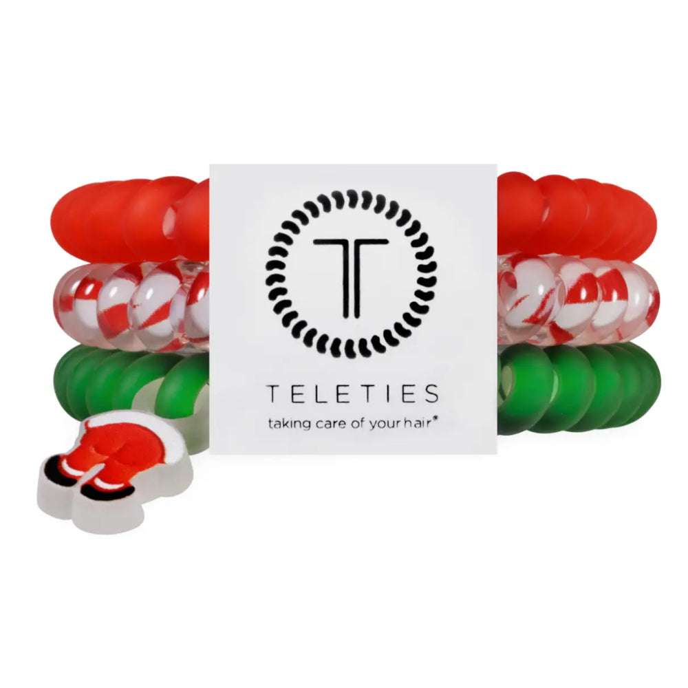 A set of silicone hair stretch bands by Teleties, featuring red, green, and red-and-white swirled bands, with a Santa Claus-themed band and a white brand card in the center.
