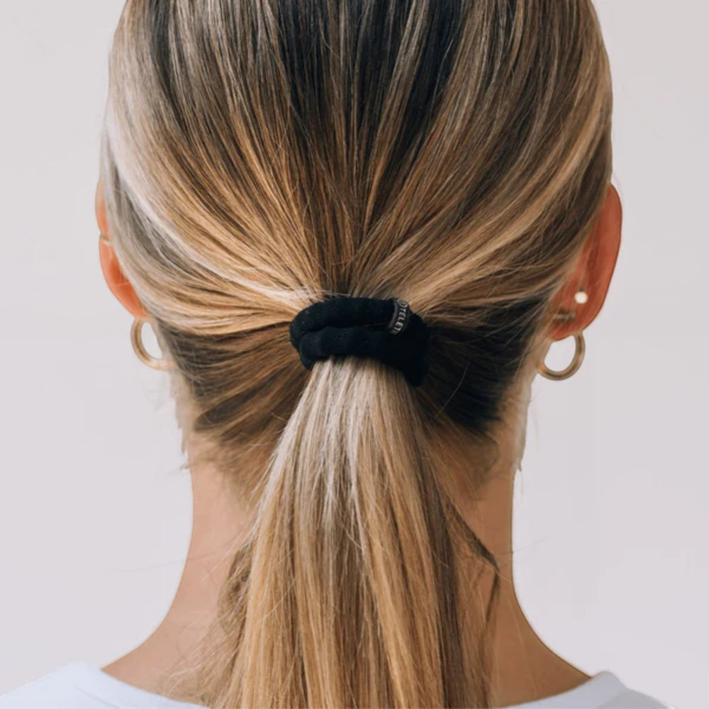 Close-up of a person with a high ponytail wearing gold hoop earrings on a plain background